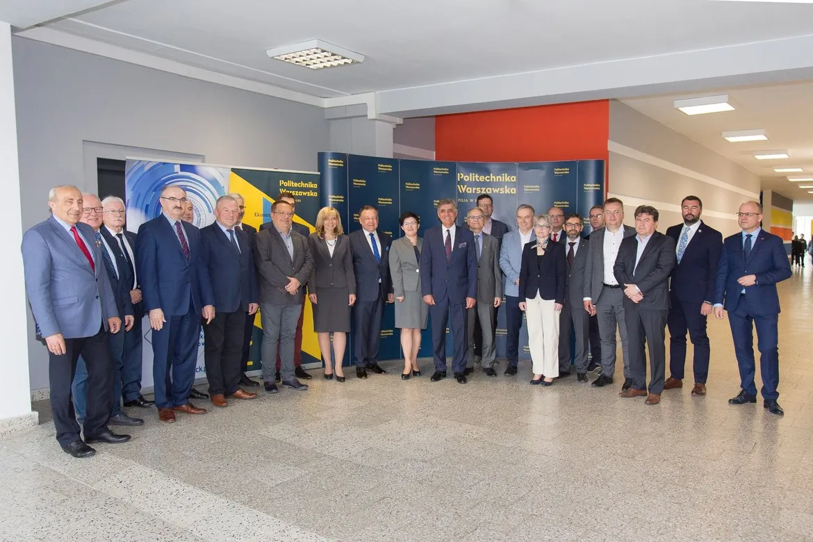 Grupa osób w garniturach stoi razem w korytarzu przed banerami Politechniki Warszawskiej podczas spotkania Rady ds. Partnerstwa Gospodarczo-Społecznego na PW.