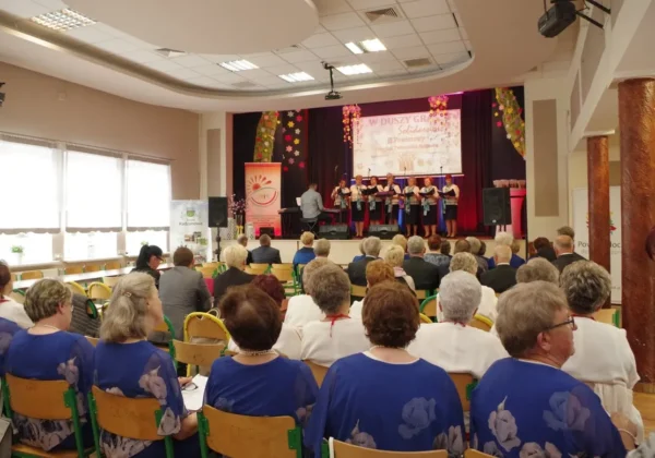 Na scenie w Radzanowie chór seniorów wykonuje występ podczas II Powiatowego Przeglądu Twórczości Seniorów, przed liczną widownią seniorów.