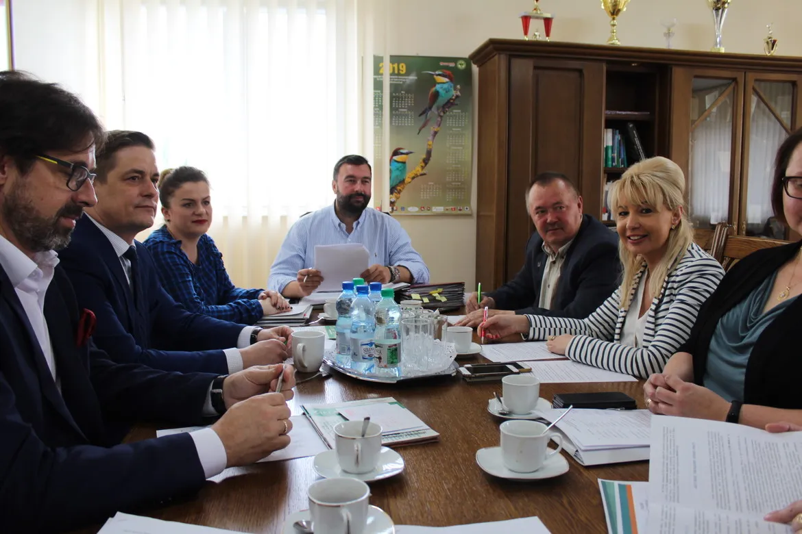 Grupa pracowników i urzędników siedzi przy stole w biurze Powiatowego Urzędu Pracy, omawiając dokumenty podczas spotkania podsumowującego ubiegły rok.