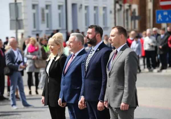 Czwórka uczestników uroczystości w formalnych garniturach stoi w rzędzie na ulicy podczas obchodów 228. rocznicy Konstytucji 3 Maja.