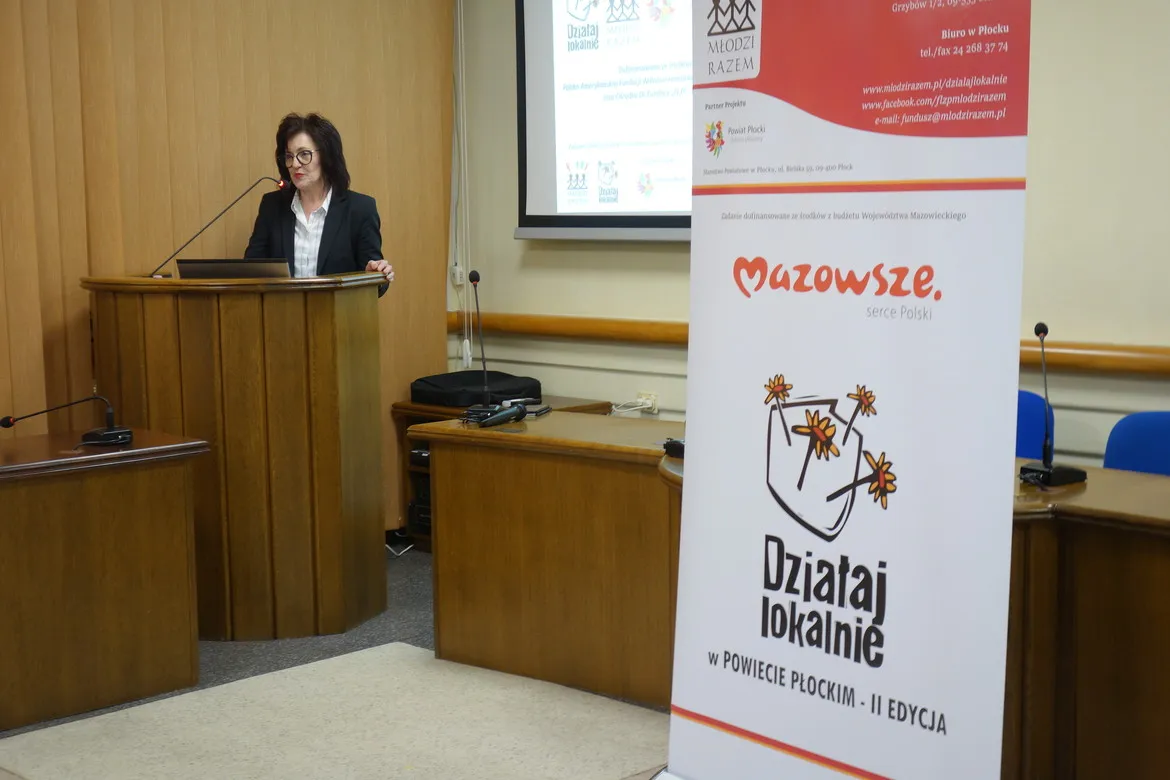 Prelegentka stoi za mównicą podczas warsztatów ws. RODO dla NGO, w sali konferencyjnej z banerami „Działaj Lokalnie” i „Mazowsze”.