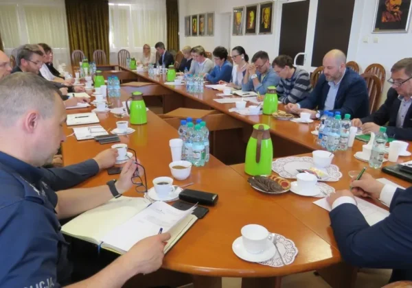 Członkowie Powiatowego Zespołu Zarządzania Kryzysowego siedzą przy dużym stole konferencyjnym i omawiają sytuację na Wiśle; mają przed sobą notatniki, filiżanki kawy i butelki wody.