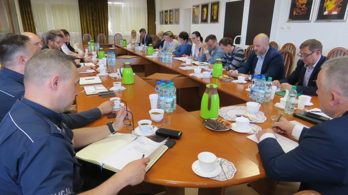 Członkowie Powiatowego Zespołu Zarządzania Kryzysowego siedzą przy dużym stole konferencyjnym i omawiają sytuację na Wiśle; mają przed sobą notatniki, filiżanki kawy i butelki wody.