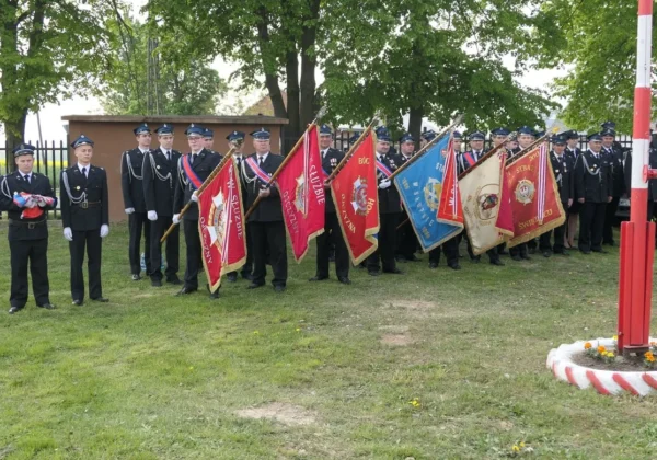Grupa strażaków w mundurach służbowych stoi w szeregu i trzyma barwne sztandary podczas Dnia Strażaka w gminie Słupno.
