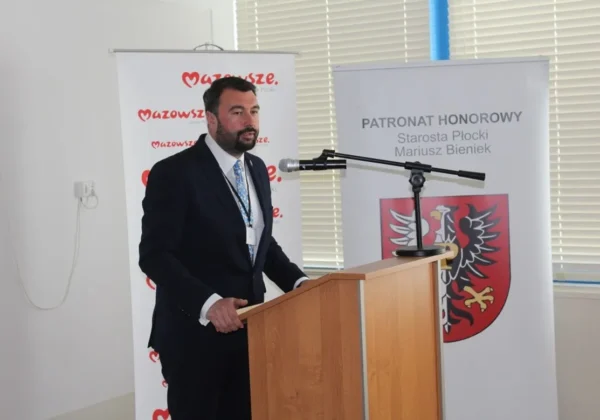 Mężczyzna w ciemnym garniturze przemawia z podiumu podczas Ogólnopolskiej Konferencji Naukowej „Pracownik nie praca, nie ucieknie? Współczesne tendencje na rynku pracy”, na tle banerów z napisem Mazowsze i herbem powiatu.
