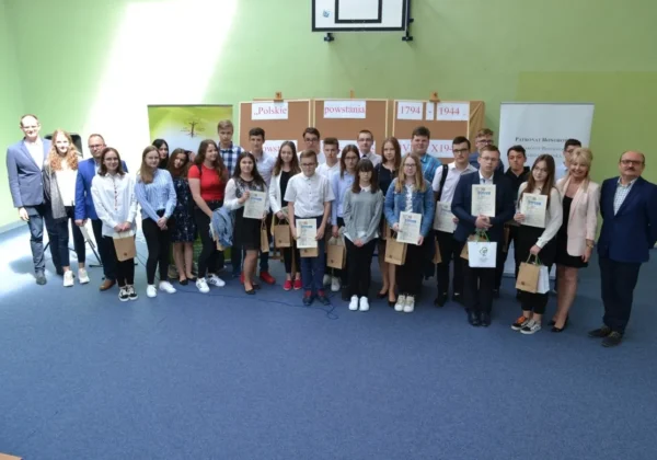 Grupa uczniów i nauczycieli stojąca razem w sali podczas wręczania nagród w konkursie historycznym „Polskie powstania 1794-1944”.