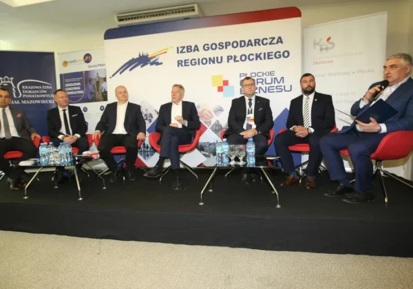 Siedmioosobowy panel dyskusyjny: mężczyźni w garniturach siedzą na czerwonych krzesłach na scenie z banerami Izby Gospodarczej Regionu Płockiego w tle.