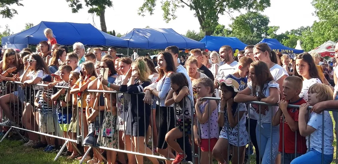 Grupa ludzi stojących za barierką podczas IX edycji Dni Bulkowa na otwartym terenie, z niebieskimi namiotami w tle.