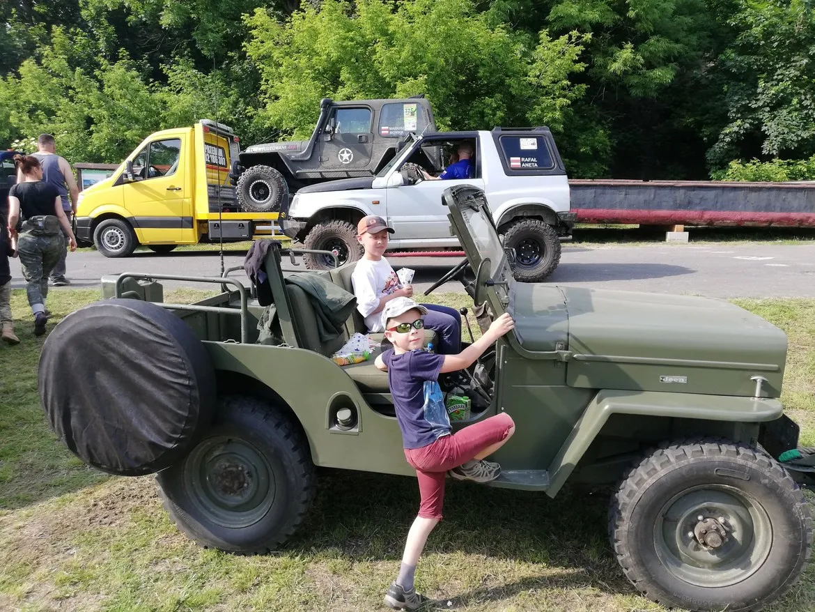 Dwoje dzieci siedzi za kierownicą zielonego terenowego jeep’a podczas prezentacji pojazdów na Terenowym Dniu Dziecka w Wyszogrądzie.