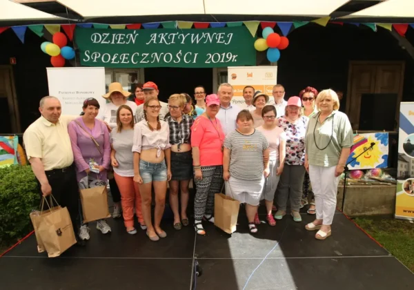 Grupa ludzi stoi na scenie przed zielonym bannerem „Dzień Aktywnej Społeczności 2019” podczas Dnia Aktywności Społecznej w brwileńskiej Antoniówce.
