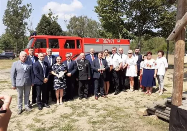 Grupa osób stojąca na placu obok czerwonego wozu strażackiego podczas Niedzieli w Lipiankach.