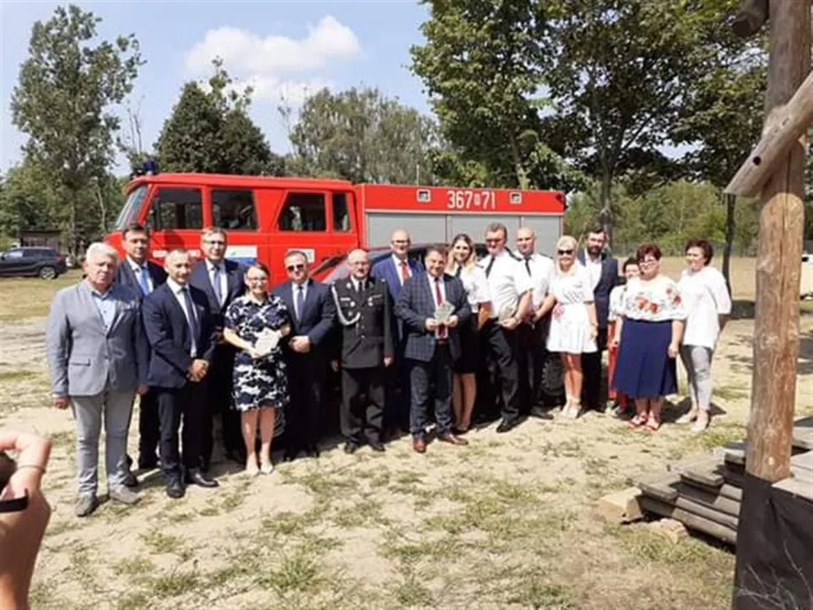 Grupa osób stojąca na placu obok czerwonego wozu strażackiego podczas Niedzieli w Lipiankach.