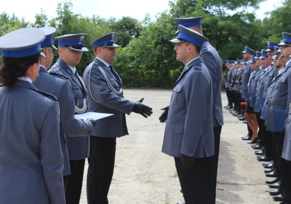 Policjanci Policji Państwowej w szarych mundurach stoją w dwóch rzędach podczas obchodów 100-lecia w Samodzielnym Pododdziale Prewencji Policji w Płocku, wymieniając uścisk dłoni.