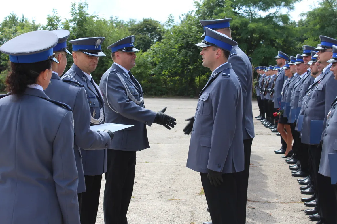 Policjanci Policji Państwowej w szarych mundurach stoją w dwóch rzędach podczas obchodów 100-lecia w Samodzielnym Pododdziale Prewencji Policji w Płocku, wymieniając uścisk dłoni.