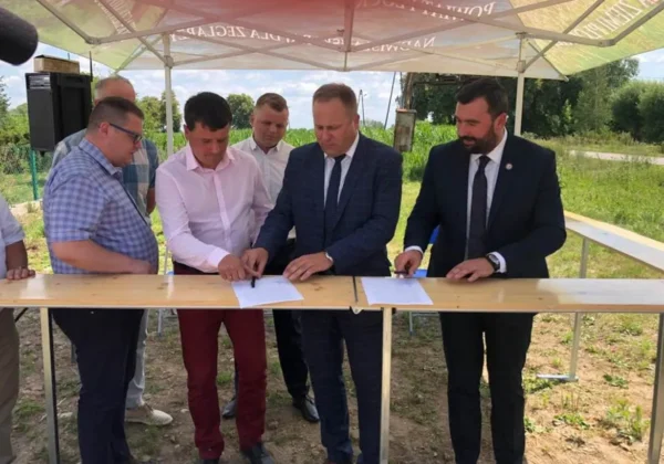 Grupa osób podpisuje dokumenty na drewnianym stole podczas ceremonii rozpoczęcia remontu ostatniego odcinka drogi Bulkowo – Worowice – granica powiatu, pod namiotem w plenerze.