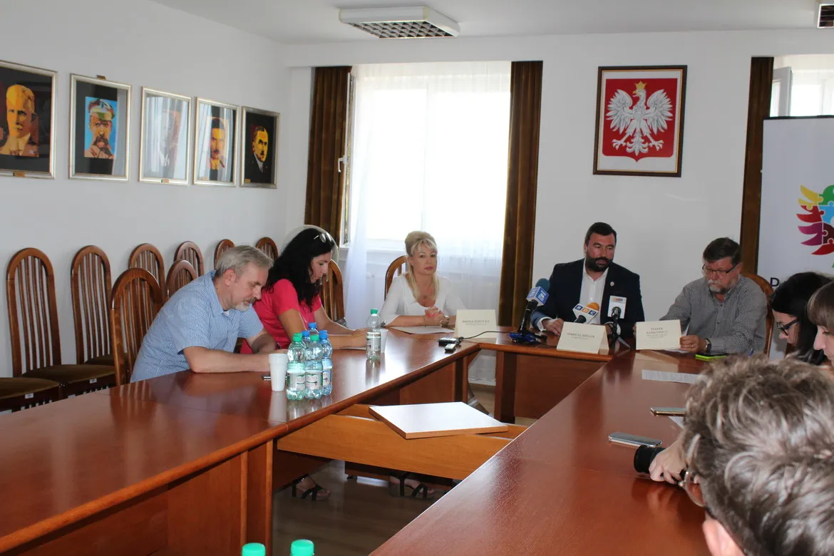 Konferencja prasowa dotycząca ASF: grupa osób siedzi przy długim stole w sali konferencyjnej, z mikrofonami, notatkami i butelkami wody.