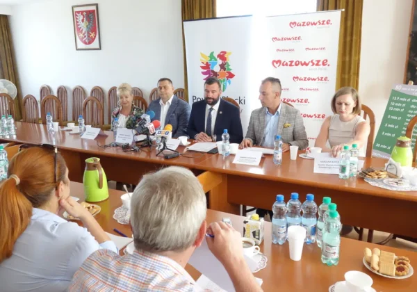 Grupa urzędników siedzi przy długim stole w sali konferencyjnej podczas konferencji prasowej promującej wsparcie Mazowsza dla Powiatu Płockiego.