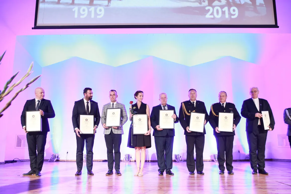 Grupa osób na scenie podczas Święta Policji w powiecie płockim, wręczająca awanse i odznaczenia oraz certyfikaty na tle kolorowego oświetlenia.