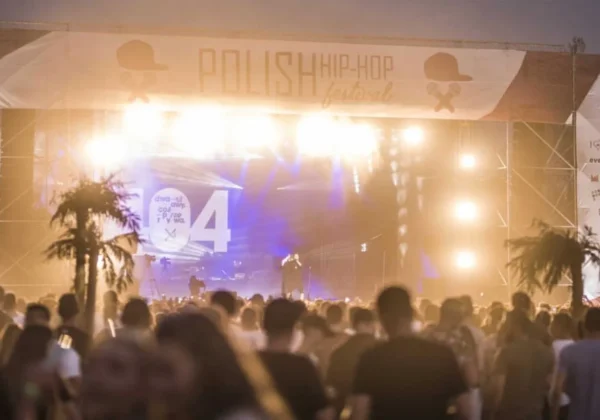 Plenerowa scena podczas PLHHF 2019 z wykonawcą na środku i tłumem widzów przed sceną, pod jasnym, kolorowym oświetleniem.