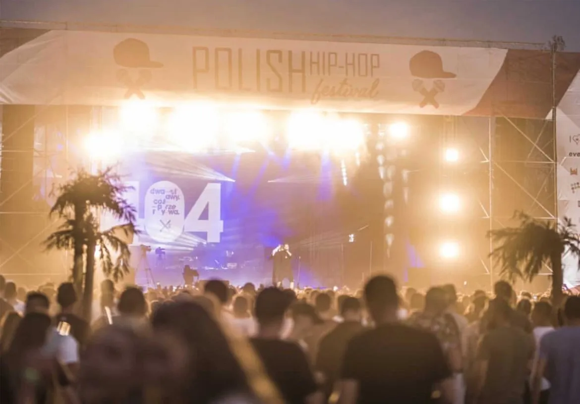 Plenerowa scena podczas PLHHF 2019 z wykonawcą na środku i tłumem widzów przed sceną, pod jasnym, kolorowym oświetleniem.