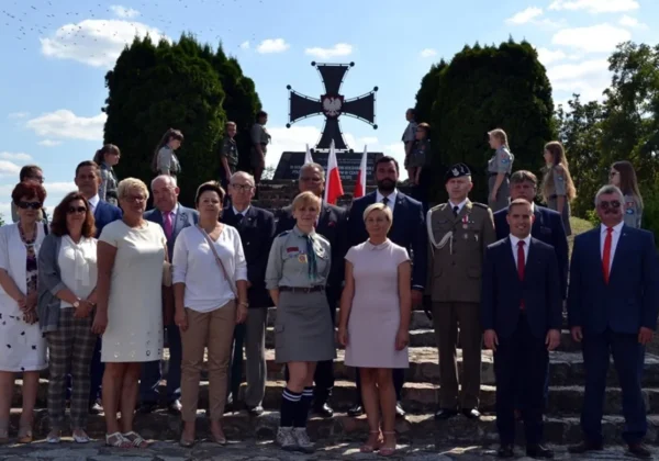 Grupa mieszkańców i osób w mundurach stoi na schodach przed pomnikiem w kształcie krzyża z orłem w centrum podczas Dni Bodzanowa 2019.