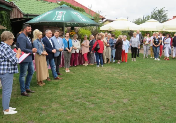 Grupa seniorów i innych uczestników stoi w rzędzie na zielonej trawie podczas festynu „Aktywny Senior nie Antyk”.