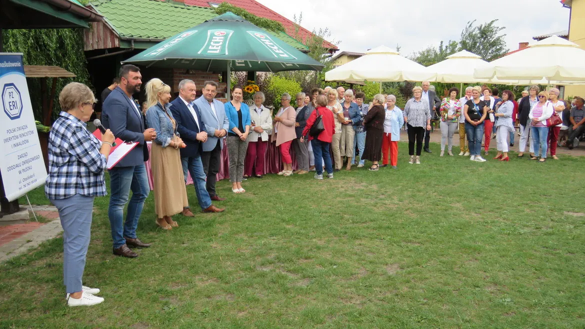 Grupa seniorów i innych uczestników stoi w rzędzie na zielonej trawie podczas festynu „Aktywny Senior nie Antyk”.
