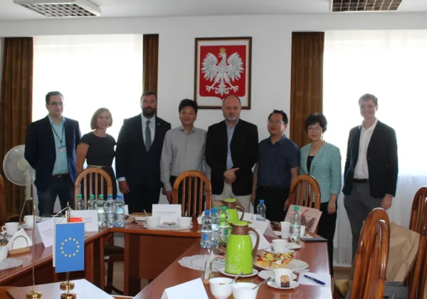 Chińska delegacja wraz z polskimi urzędnikami stoi przy stole konferencyjnym podczas wizyty w powiecie płockim.
