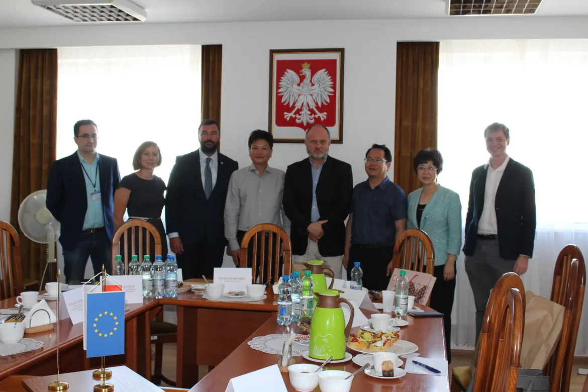 Chińska delegacja wraz z polskimi urzędnikami stoi przy stole konferencyjnym podczas wizyty w powiecie płockim.