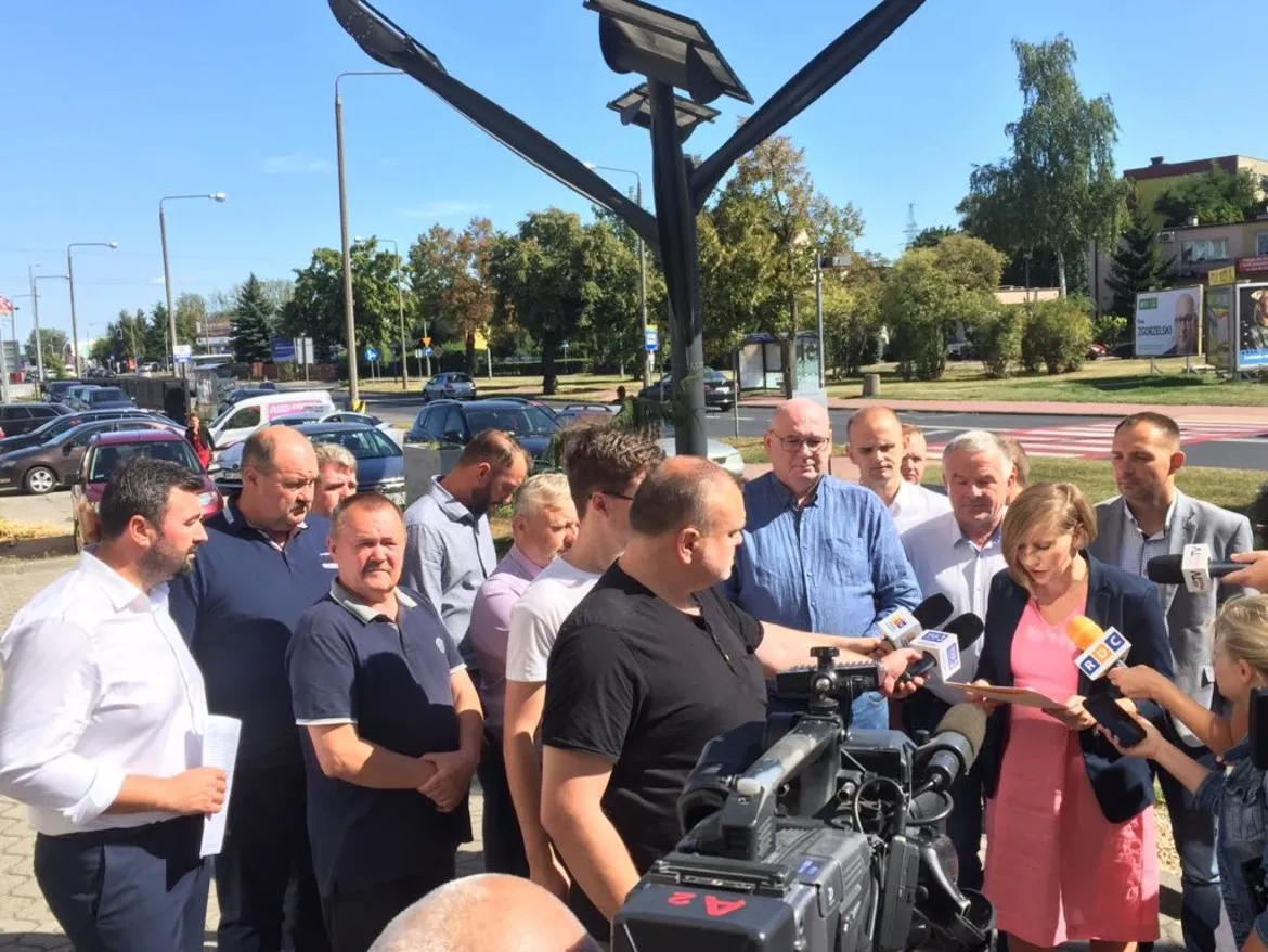 Grupa osób, w tym dziennikarze z mikrofonami i kamerą, prowadzi konferencję prasową na temat ASF przed płockim Starostwem.