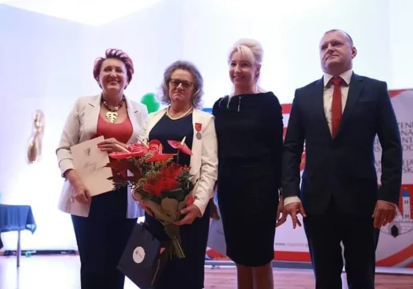 Cztery osoby stoją na scenie podczas uroczystości z okazji 20-lecia pomocy chorym na Alzheimera; jedna z kobiet trzyma bukiet kwiatów i dokumenty.