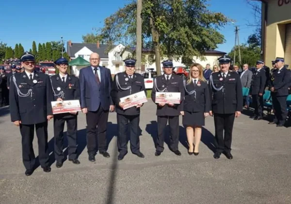 Grupa strażaków OSP Bielsk w mundurach galowych stoi na placu, trzymając certyfikaty podczas jubileuszowej uroczystości 110-lecia istnienia jednostki.