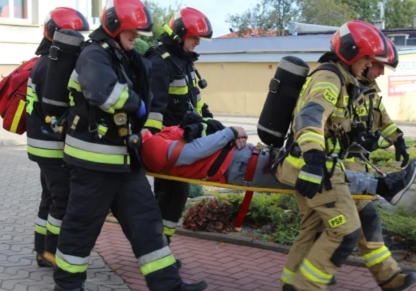 Grupa strażaków w hełmach i ubraniach ochronnych niesie na noszach rannego podczas ćwiczeń obronnych Zielony Jar 2019.