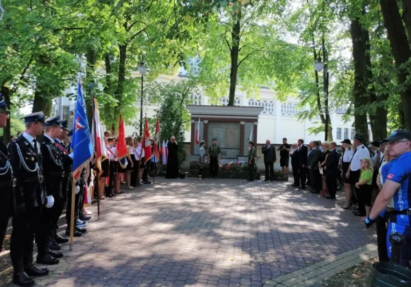 Uczestnicy obchodów 80. rocznicy wybuchu II wojny światowej w Gąbinie stoją po obu stronach alejki przed centralnym pomnikiem, trzymając flagi.