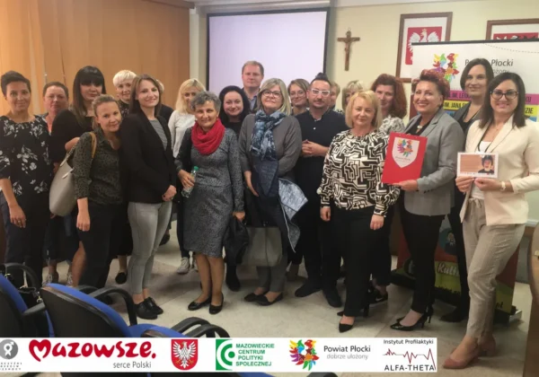 Grupa uczestników konferencji w sali, stojących razem podczas prezentacji projektu Punkt Profilaktyczno–Konsultacyjny dla osób podejmujących zachowania ryzykowne z terenu powiatu płockiego.