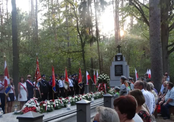 Uroczystość upamiętniająca wybuch II wojny światowej w Powiecie Płockim: uczestnicy w mundurach i strojach cywilnych stoją przed pomnikiem, otoczeni flagami i wieńcami.