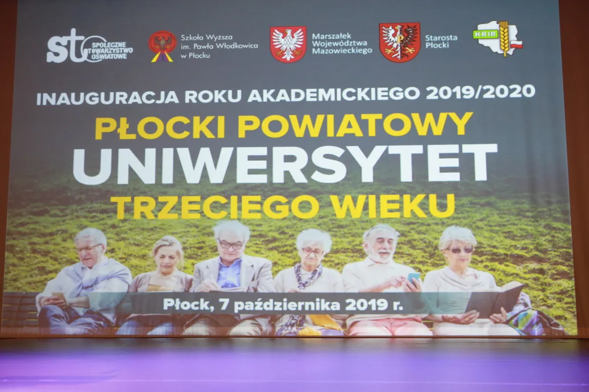 Plakat inaugurujący rok akademicki 2019/2020 Płockiego Powiatowego Uniwersytetu Trzeciego Wieku, na którym grupa seniorów siedzi na ławce na tle zielonej łąki.