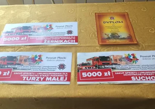 Na stole leżą dokumenty i dyplom potwierdzające wsparcie finansowe w wysokości 5000 zł dla jednostek Ochotniczych Straży Pożarnych.