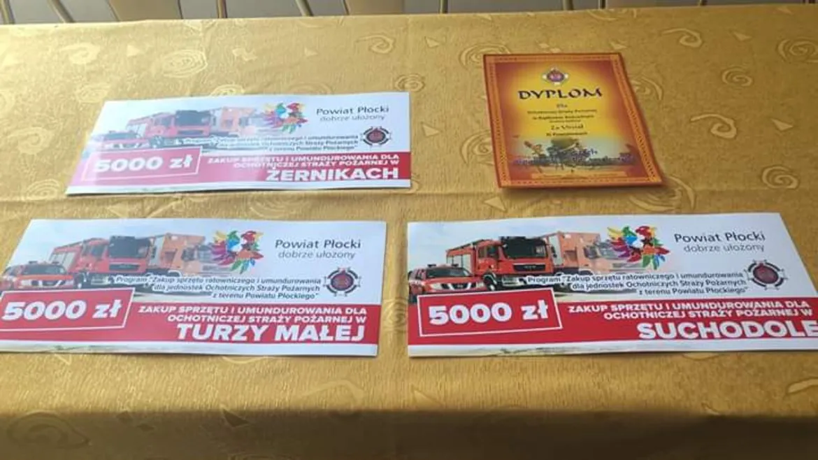 Na stole leżą dokumenty i dyplom potwierdzające wsparcie finansowe w wysokości 5000 zł dla jednostek Ochotniczych Straży Pożarnych.