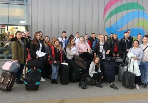 Grupa 26 uczniów Zespołu Szkół im. Jana Śniadeckiego w Wyszogrodzie stoi z walizkami przed nowoczesnym budynkiem z kolorowym muralem, przygotowując się do wyjazdu w ramach ERASMUS+ vol 1.