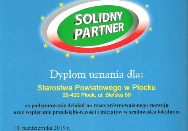 Niebieski plakat z hasłem „Solidny partner w środowisku lokalnym” i logotypem „Solidny Partner” oraz informacją o wyróżnieniu Starostwa Powiatowego w Płocku w 2019 roku.