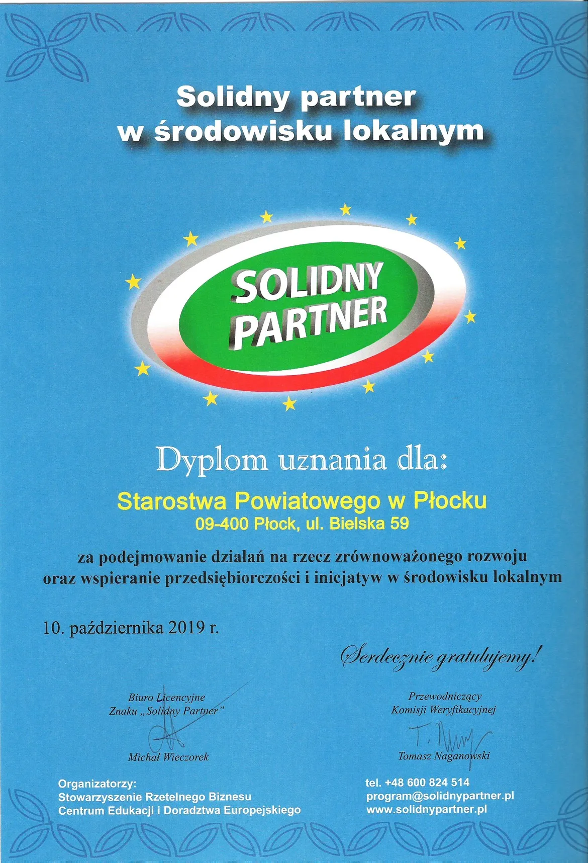 Niebieski plakat z hasłem „Solidny partner w środowisku lokalnym” i logotypem „Solidny Partner” oraz informacją o wyróżnieniu Starostwa Powiatowego w Płocku w 2019 roku.