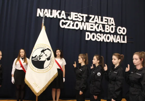 Grupa uczniów klas pierwszych w szkolnych mundurach składa przysięgę podczas obchodów Święta Patrona Szkoły w Zespole Szkół im. Jana Śniadeckiego w Wyszogrodzie, przy sztandarze szkoły.