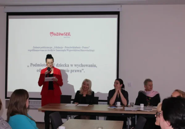 Prelegentka w czerwonym garniturze przemawia do publiczności z mikrofonem podczas konferencji, na ekranie w tle widnieje tytuł „Podmiotowość dziecka w wychowaniu, edukacji i systemie prawa”.