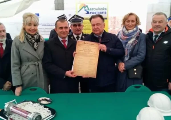 Grupa osób w formalnych ubraniach stoi podczas uroczystości w Siecieniu, trzymając dokument potwierdzający wmurowanie kamienia węgielnego pod budowę Strażnicy OSP i świetlicy wiejskiej.