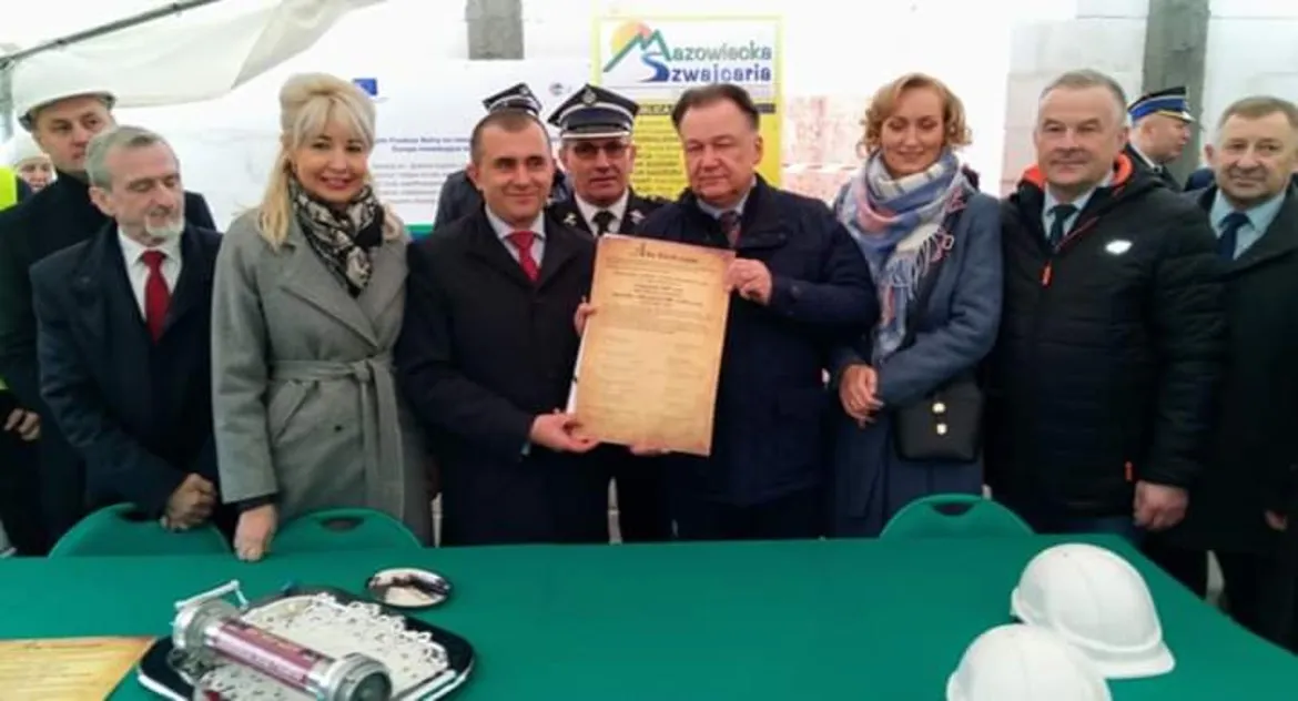 Grupa osób w formalnych ubraniach stoi podczas uroczystości w Siecieniu, trzymając dokument potwierdzający wmurowanie kamienia węgielnego pod budowę Strażnicy OSP i świetlicy wiejskiej.