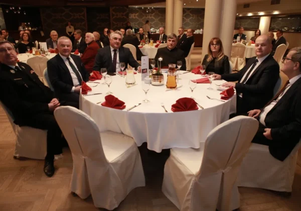 Grupa gości w garniturach siedzi przy okrągłym stole podczas wigilijnego spotkania w IGRP, z czerwonymi serwetkami i kieliszkami na stole.