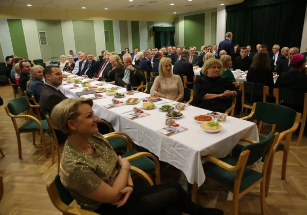 Uczestnicy spotkania opłatkowego Solidarności w Płocku siedzą przy długim stole zastawionym potrawami i napojami w sali konferencyjnej.