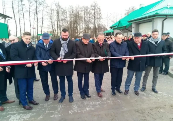 Grupa mężczyzn w eleganckich płaszczach i kurtkach przecina czerwono-białą wstęgę podczas otwarcia nowoczesnej oczyszczalni ścieków w Bodzanowie.