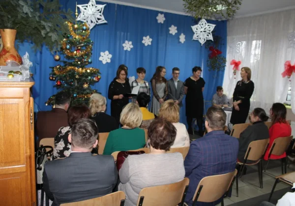 Grupa osób stoi na scenie podczas wigilijnego spotkania w Wyszogrodzie, przed publicznością, a za nimi w tle widoczna choinka i świąteczne dekoracje.